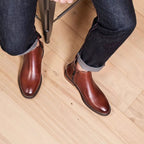 Dark brown leather pointed-toe dress boots with side zipper, worn over jeans.