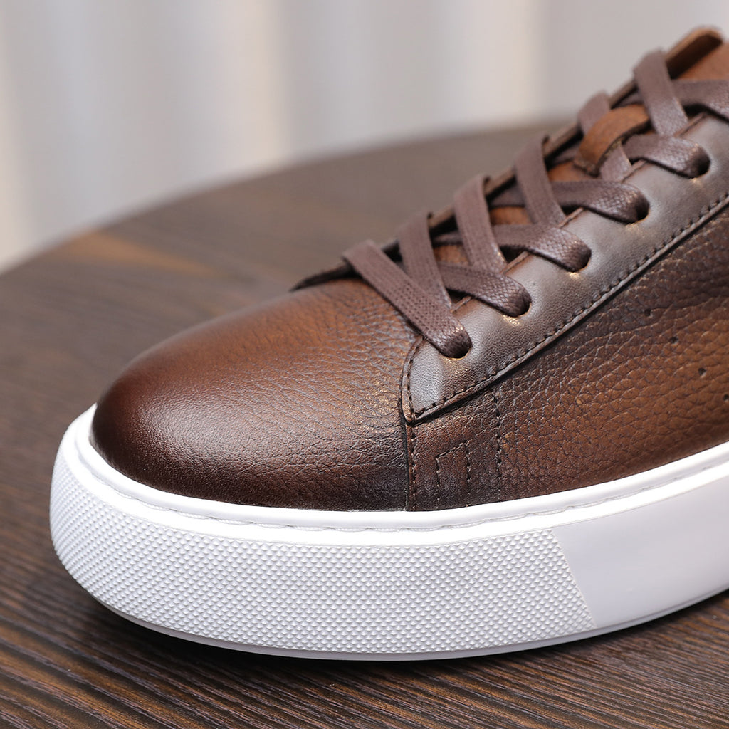 Close-up of dark brown leather sneaker toe with lace eyelets and white sole edge.