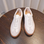 White leather sneakers close-up showing laces, toe shape, and tan trim