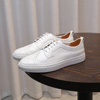 Men's genuine leather sneakers, white lace-up pair with perforated toe and stitched side panels.