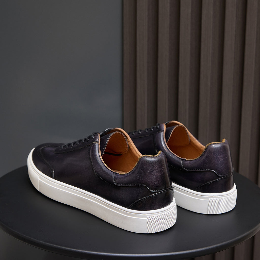 Men's leather sneakers, dark black with white sole and tan lining at the collar.