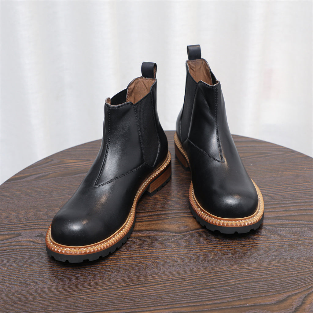 Black Chelsea boots with pointed toe, elastic side panels, and tan welt on lug sole