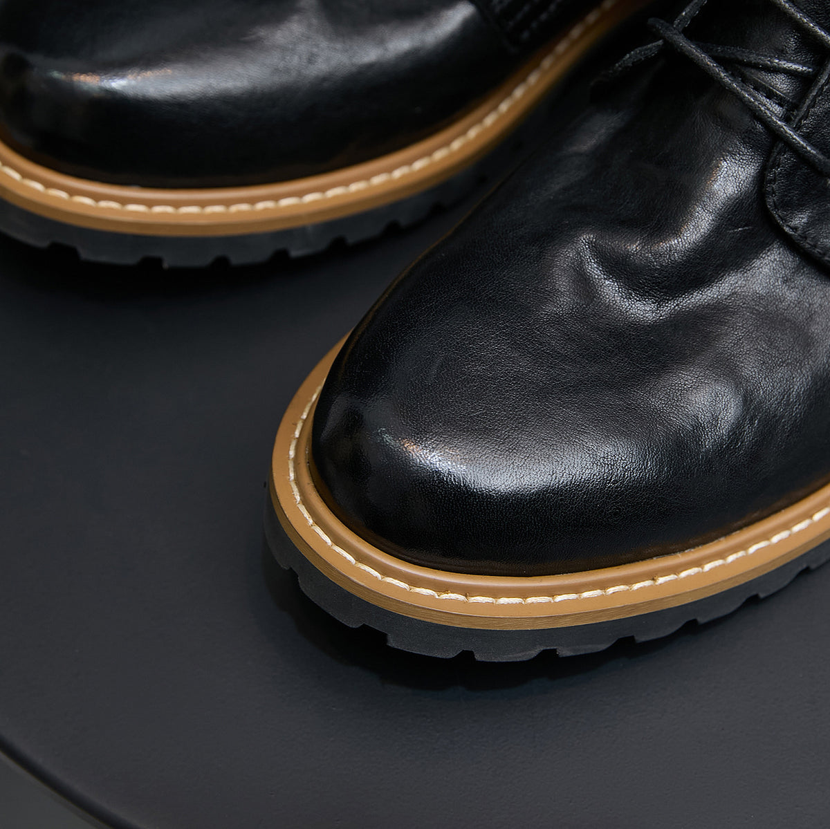 Black leather pointed-toe ankle boot with lace-up and side zipper detail.