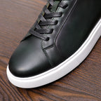 Close-up of men's dark leather sneaker with black laces, stitching detail, white sole