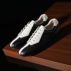 Black and white leather sneakers with lace-up front, on a wooden platform.