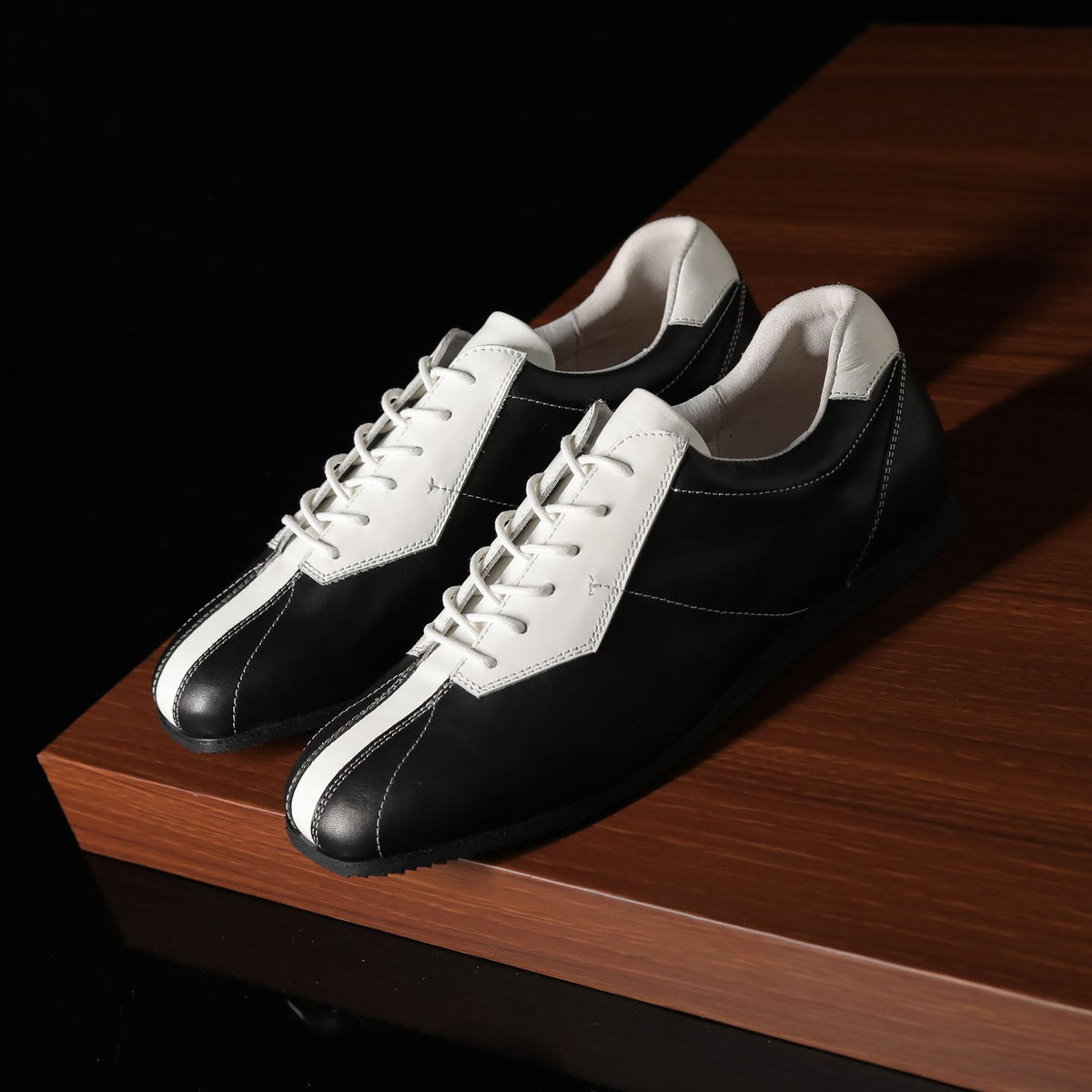 Black and white leather sneakers with lace-up front, on a wooden platform.