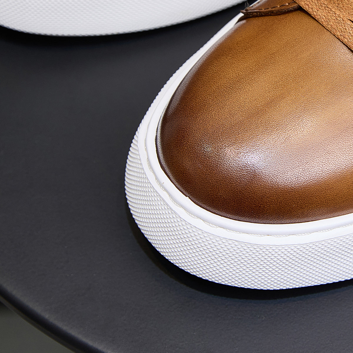 Men's brown leather sneaker toe and textured white midsole edge in close-up
