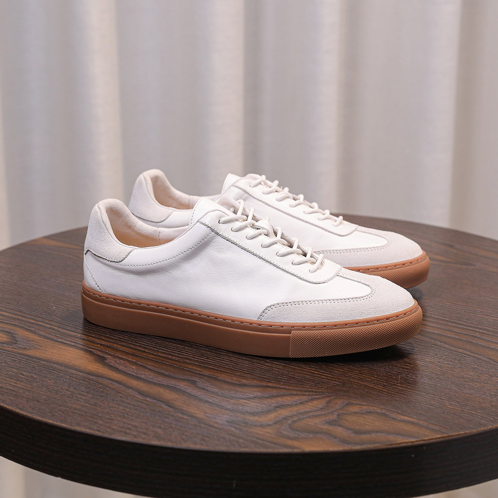 White leather lace-up sneakers with tan sole, side profile on table