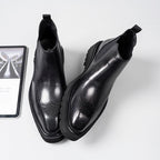 Black leather Chelsea dress boots with elastic gore, brogue-style perforations, angled view