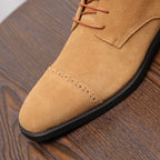 Tan suede chukka boot toe and lace panel with perforations and black sole