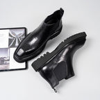 Black leather Chelsea dress boots with elastic gore, perforated toe, chunky tread sole