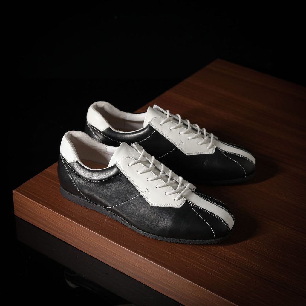 Pair of black and white leather sneakers, side view with lace-up design.
