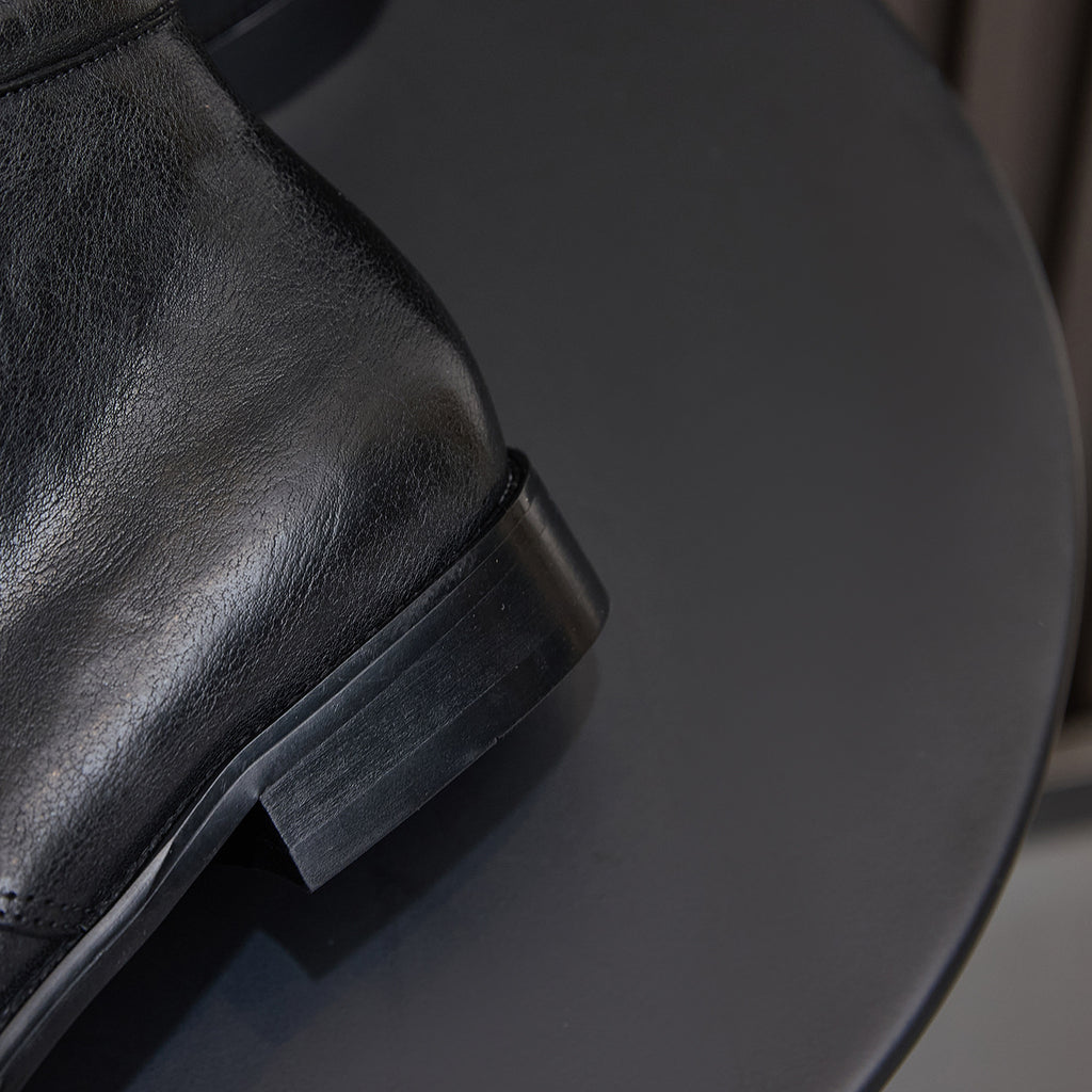 Black leather lace-up chukka boot, close-up of ankle panel and outsole edge.