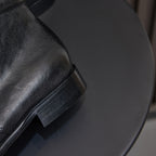 Black leather lace-up chukka boot, close-up of ankle panel and outsole edge.