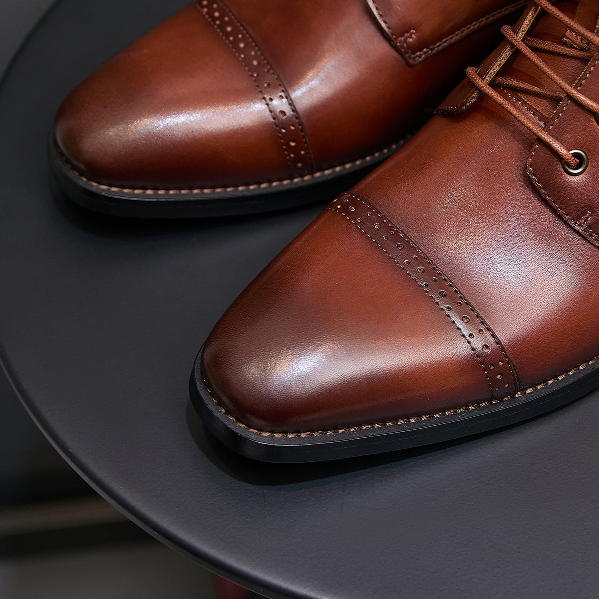 Men's brown leather pointed-toe boots showing lace eyelets and stitched trim on toe