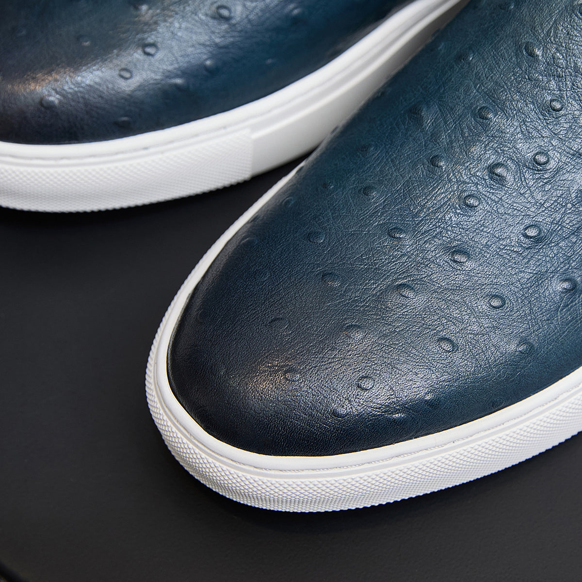 Men's blue leather slip-on sneaker close-up with white sole and textured surface