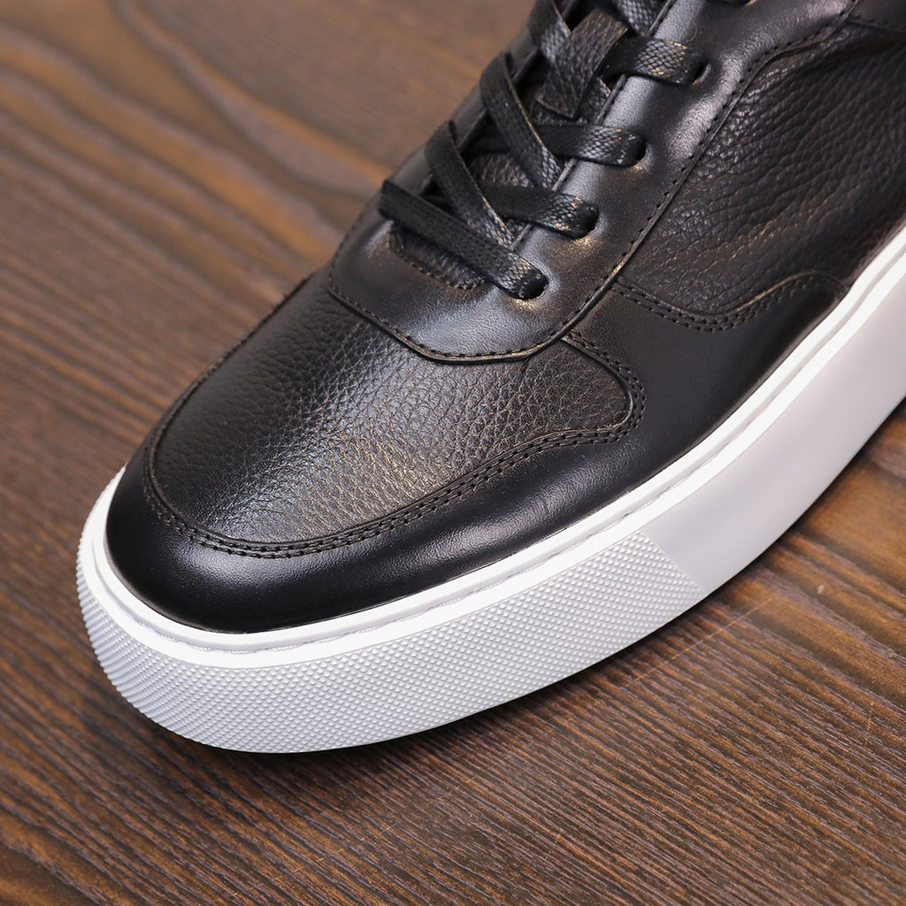 Men's leather sneakers, black, close-up of lace area and white outsole edge.