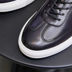 Close-up of dark leather sneaker with black laces, stitched panels, and white sole.
