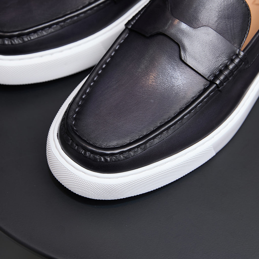 Close-up of black leather slip-on sneakers with moccasin stitching and white platform sole