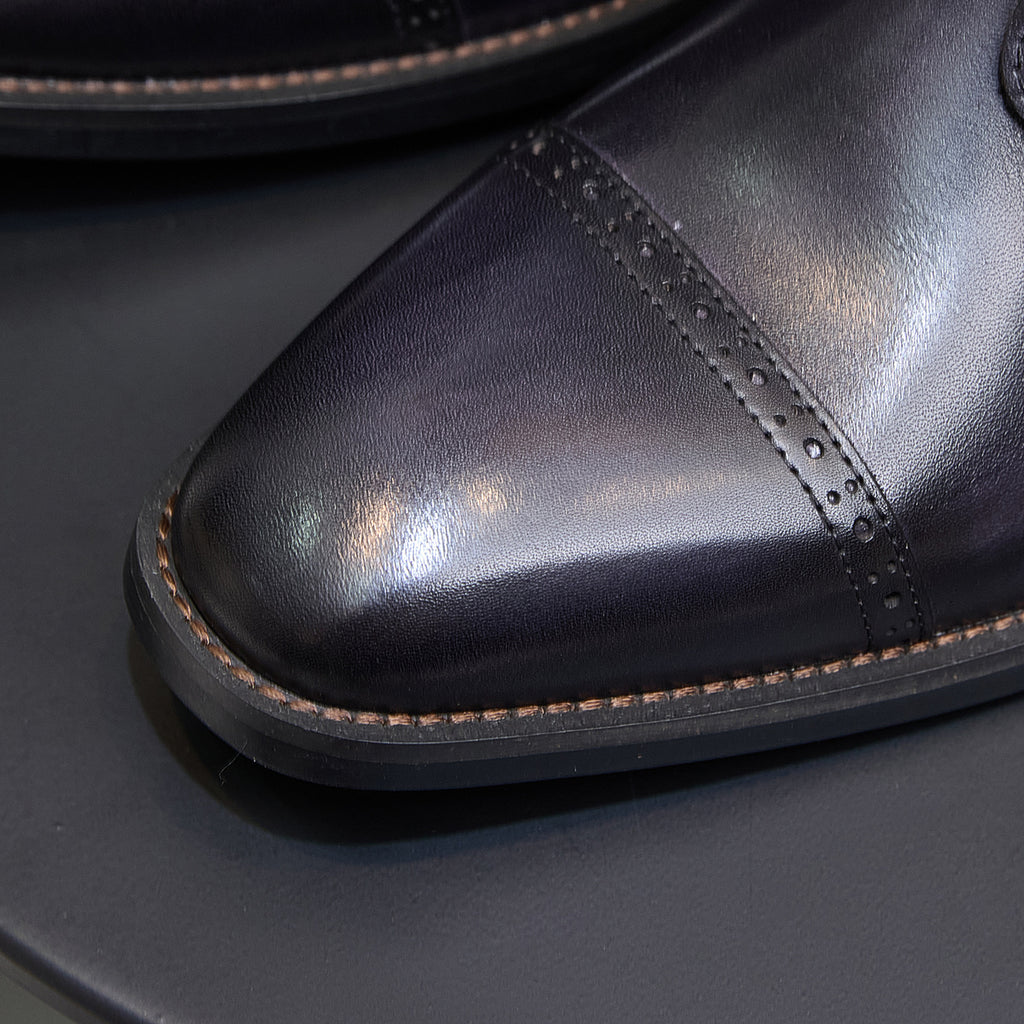 Leather boot toe with pointed cap and brogue-style perforations, dark blue finish.