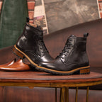 Pair of black pointed-toe leather ankle boots with lace-up and side-zip, on wooden stand.