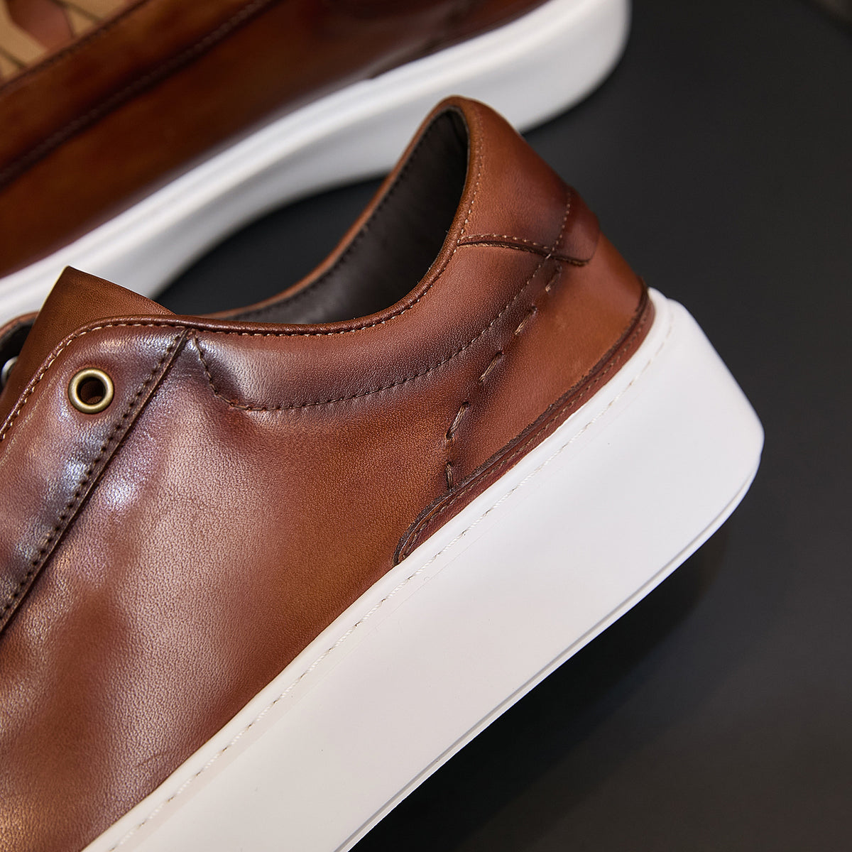Brown leather sneaker side panel with stitching and round metal eyelet