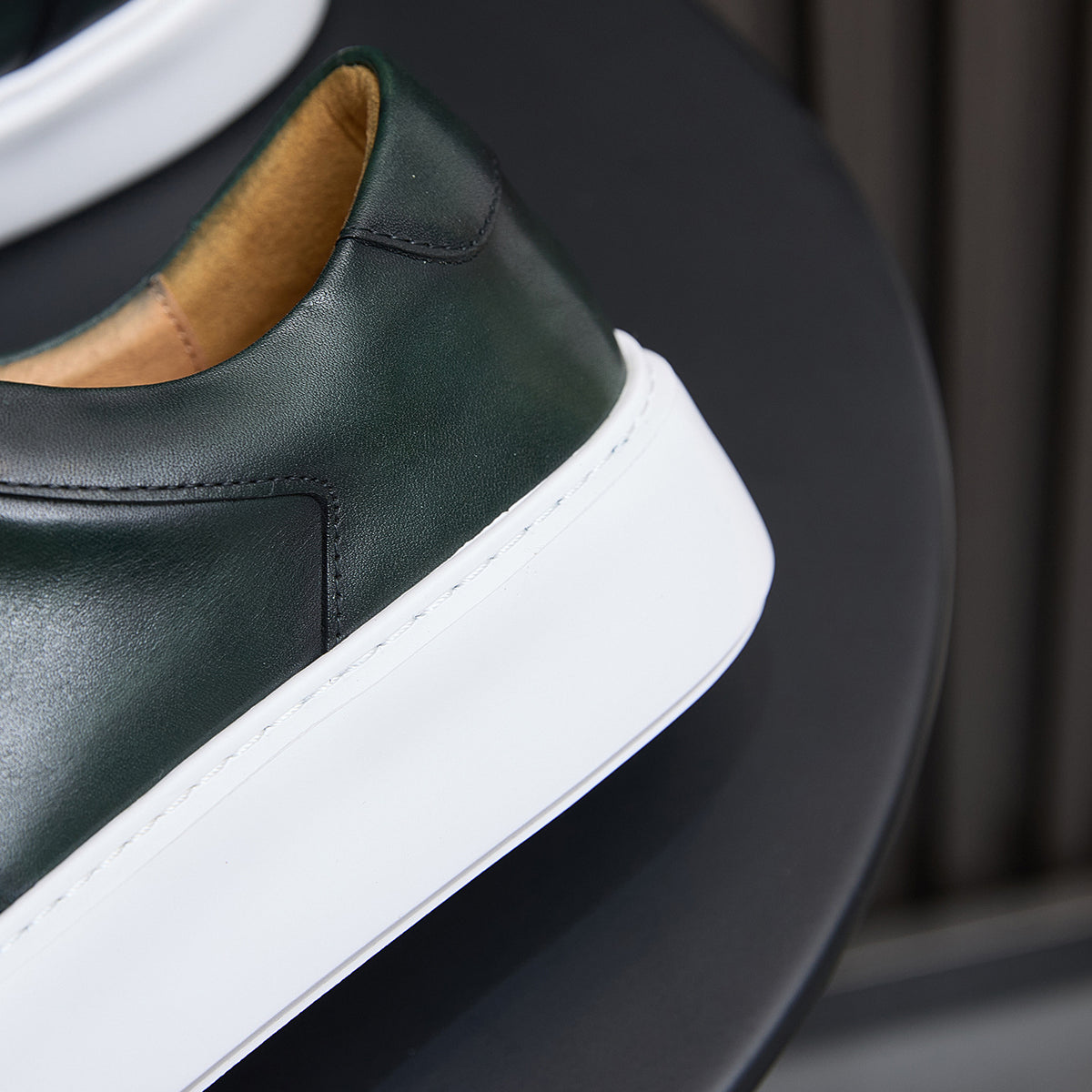Leather sneakers side close-up, dark green upper with white midsole and tan lining.
