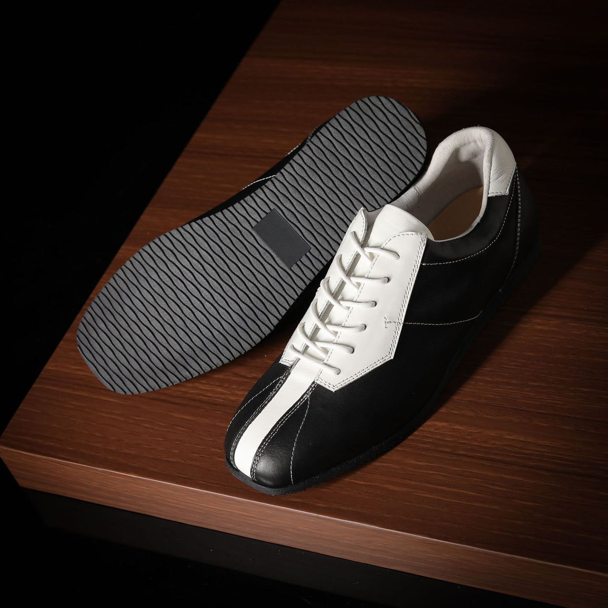 Black and white leather sneakers showing textured rubber outsole tread.