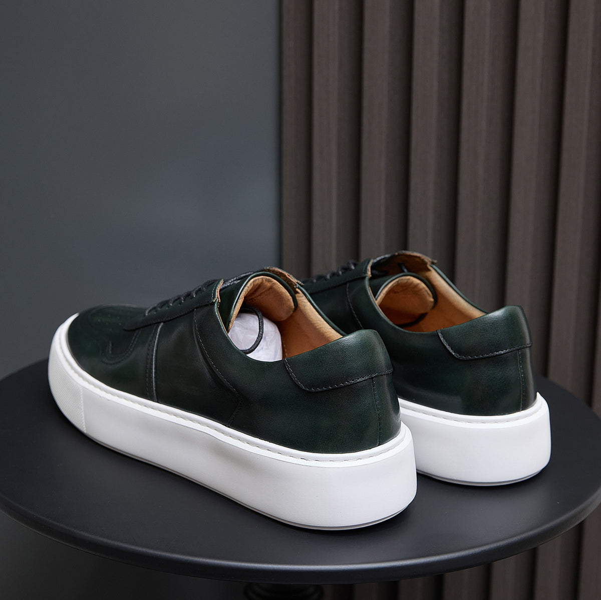 Leather sneakers rear view, dark green uppers with heel tabs and white rubber sole.