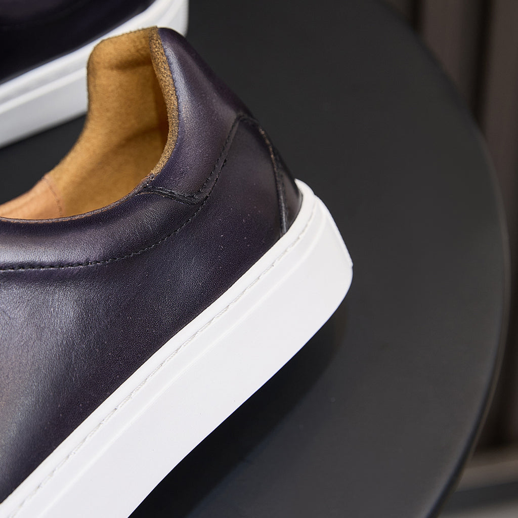 Side view close-up: dark purple leather sneaker with tan lining and thick white sole.