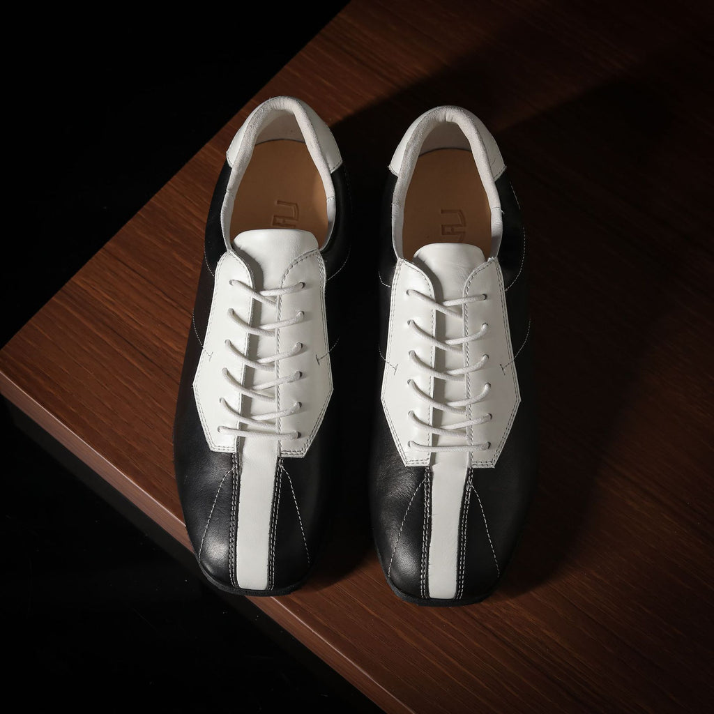 Black and white leather sneakers, top view with white laces and open collar.