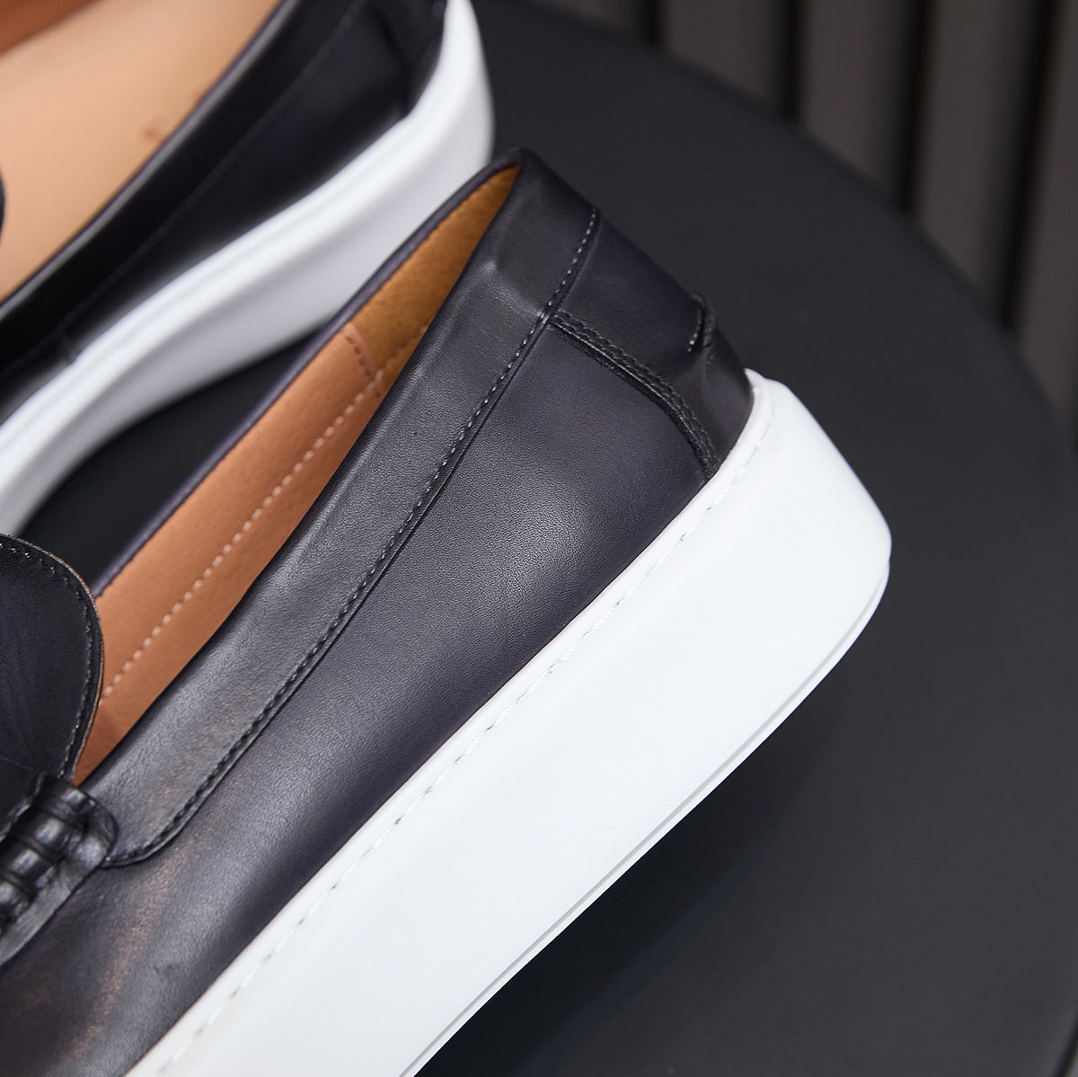 Close-up of black leather slip-on sneaker upper with tan interior and white platform sole