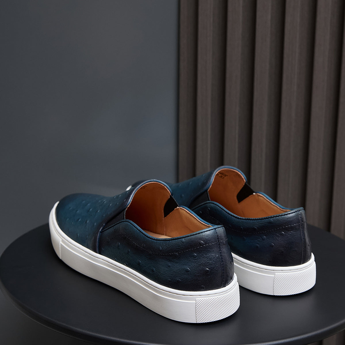 Men's dark blue slip-on leather sneakers with white soles, rear angle view