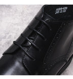 Black lace-up dress boots with wingtip perforations and textured leather upper
