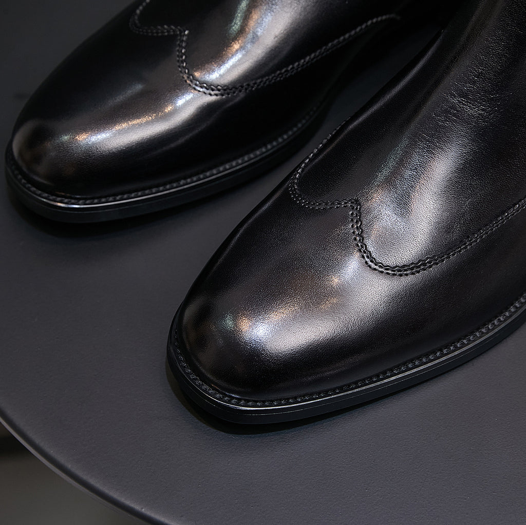 Close-up of men's pointed-toe black chelsea boots with stitched seam and glossy finish