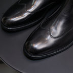 Close-up of men's pointed-toe black chelsea boots with stitched seam and glossy finish