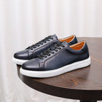 Men's dark leather lace-up sneakers with white outsole, pair on round wooden tabletop