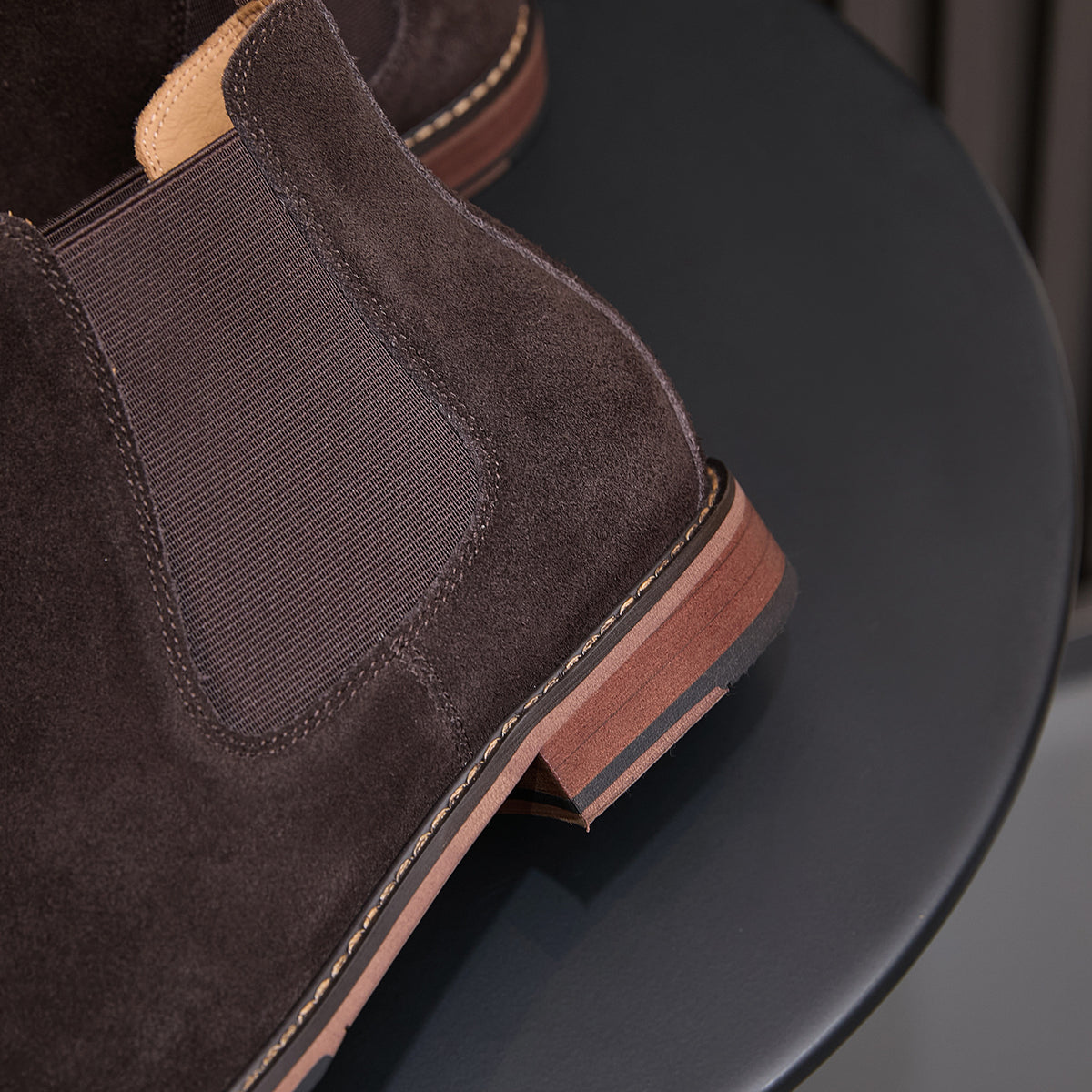 Close-up of dark brown suede Chelsea boot side elastic and low wooden-look heel