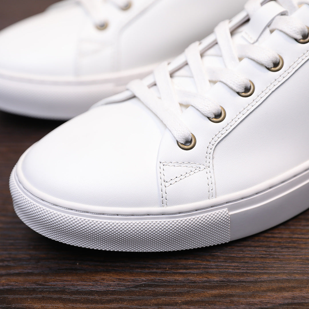 Men's white leather sneakers close-up, lace-up front and textured rubber sole.