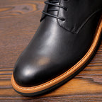 Black leather pointed toe boot with orange welt trim on a wooden surface