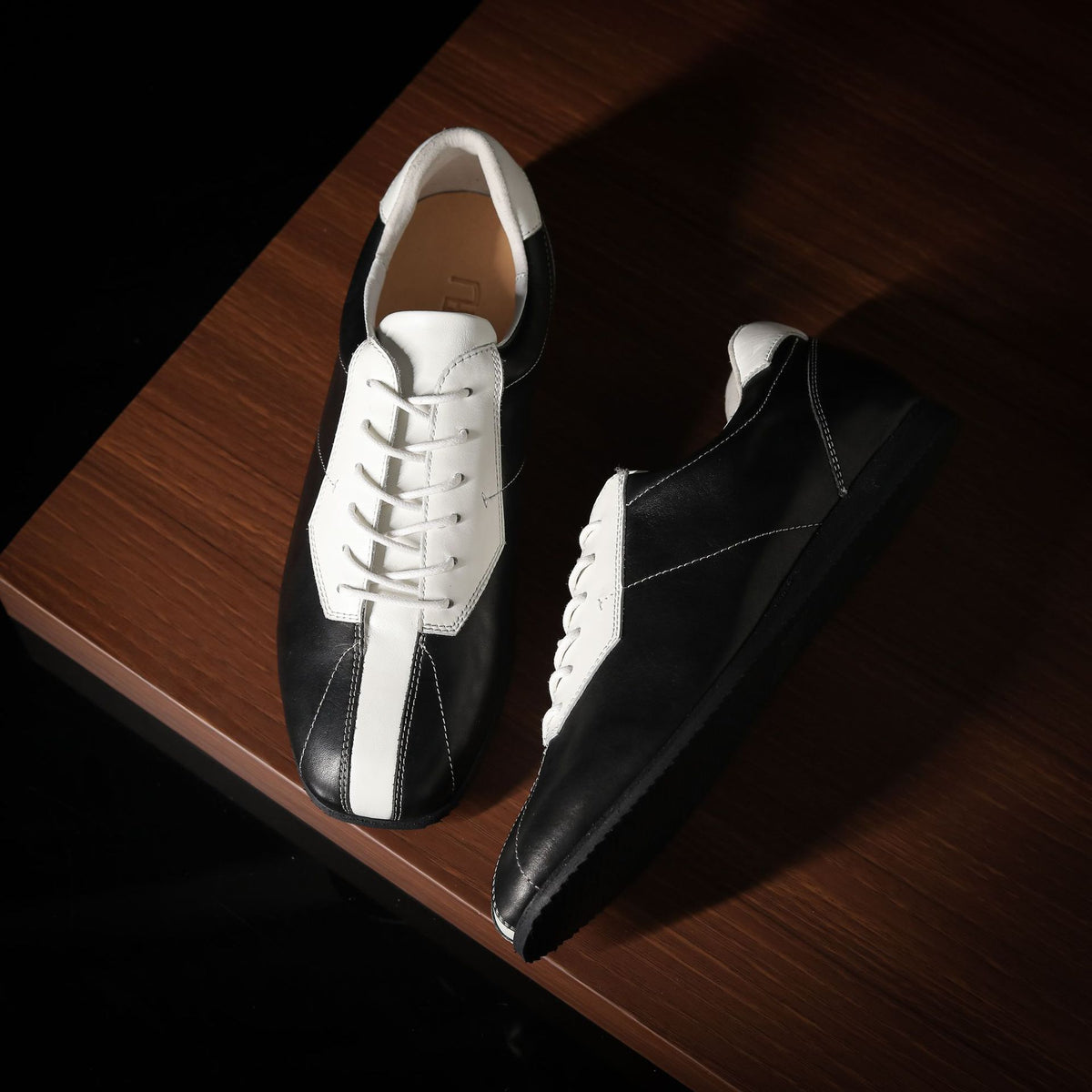 Black and white leather sneakers, angled view showing toe and side panel stitching.