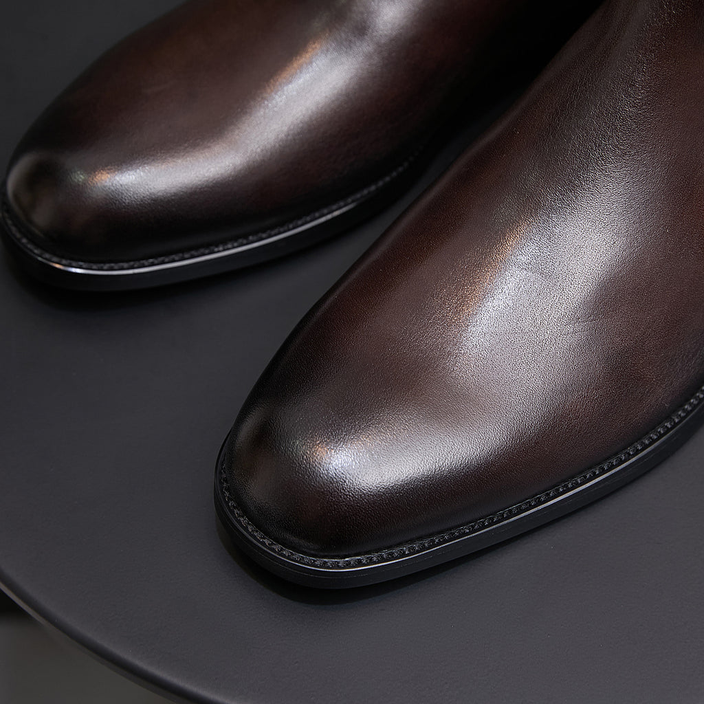 Close-up of men's pointed-toe dark brown leather dress boots with stitched welt.