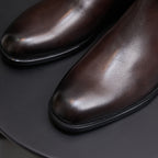 Close-up of men's pointed-toe dark brown leather dress boots with stitched welt.