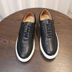Pair of black leather sneakers, lace-up front view with white sole and perforated toe