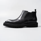 Black leather Chelsea dress boot profile with elastic gore, perforations, and tread sole