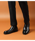 Men's black leather chelsea dress boots worn with dark pants, slip-on elastic panels.