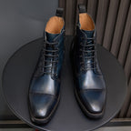 Two lace-up leather ankle boots with dark blue finish, pointed toe and tan lining.