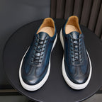 Front view of men's blue leather sneakers with black laces, white sole, and tan lining.