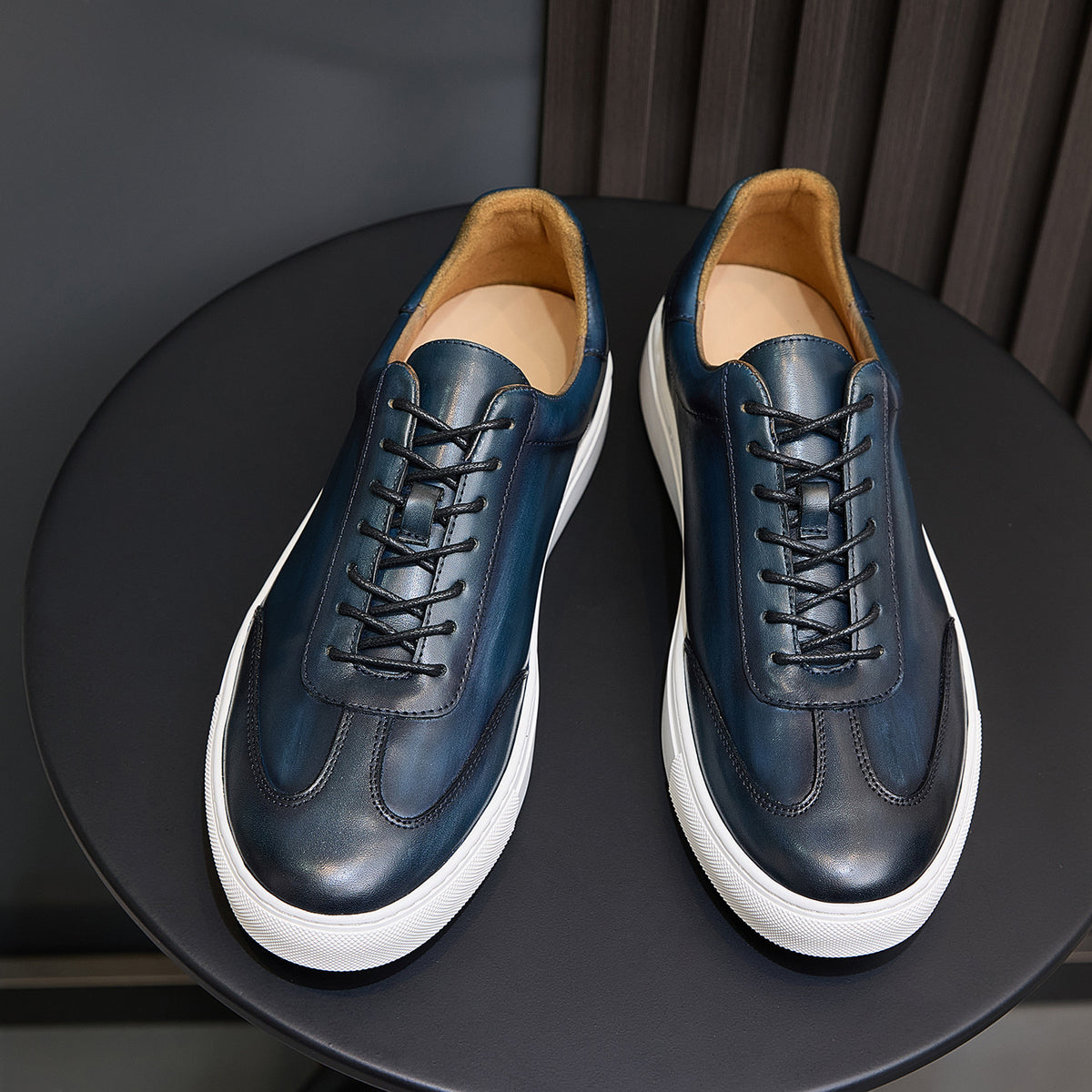 Front view of men's blue leather sneakers with black laces, white sole, and tan lining.