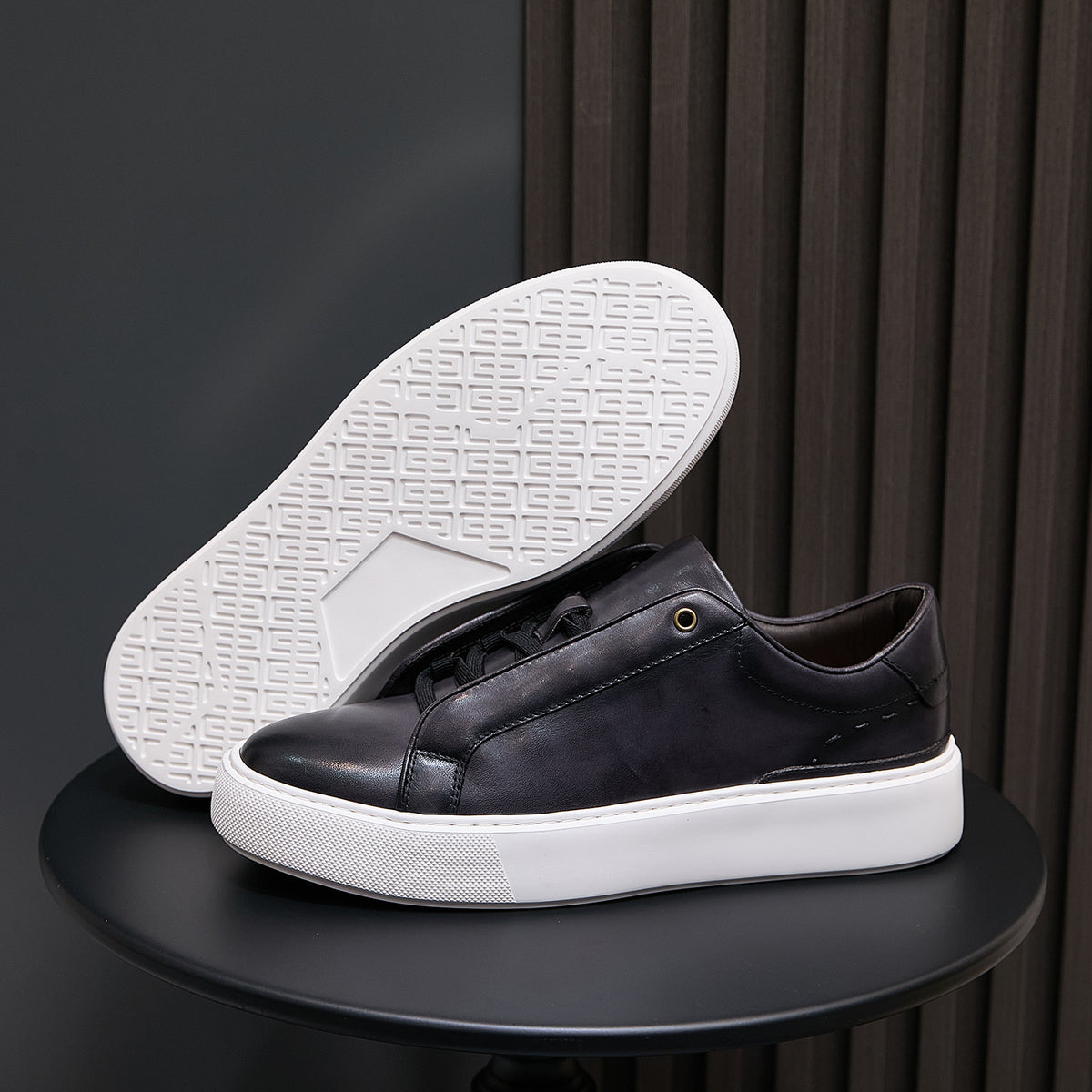 Black leather sneakers showing white outsole with grid tread pattern